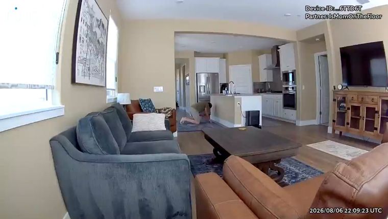 A still image from a Ring camera: a person on hands and knees on the living-room floor near the kitchen