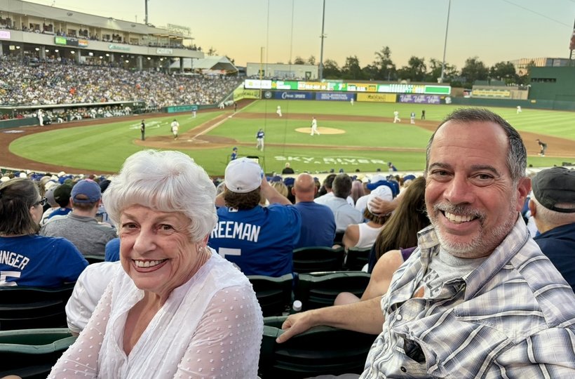 Lance Walley and his step-mom smiling in the stands at a baseball game, the field behind them