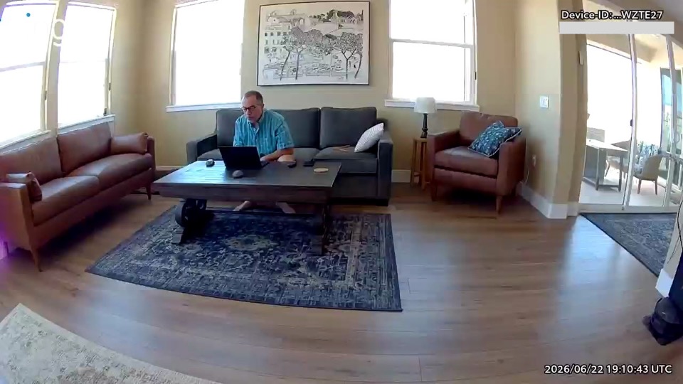 A person sitting on the front edge of a sofa, leaning forward over a coffee table to use a laptop.